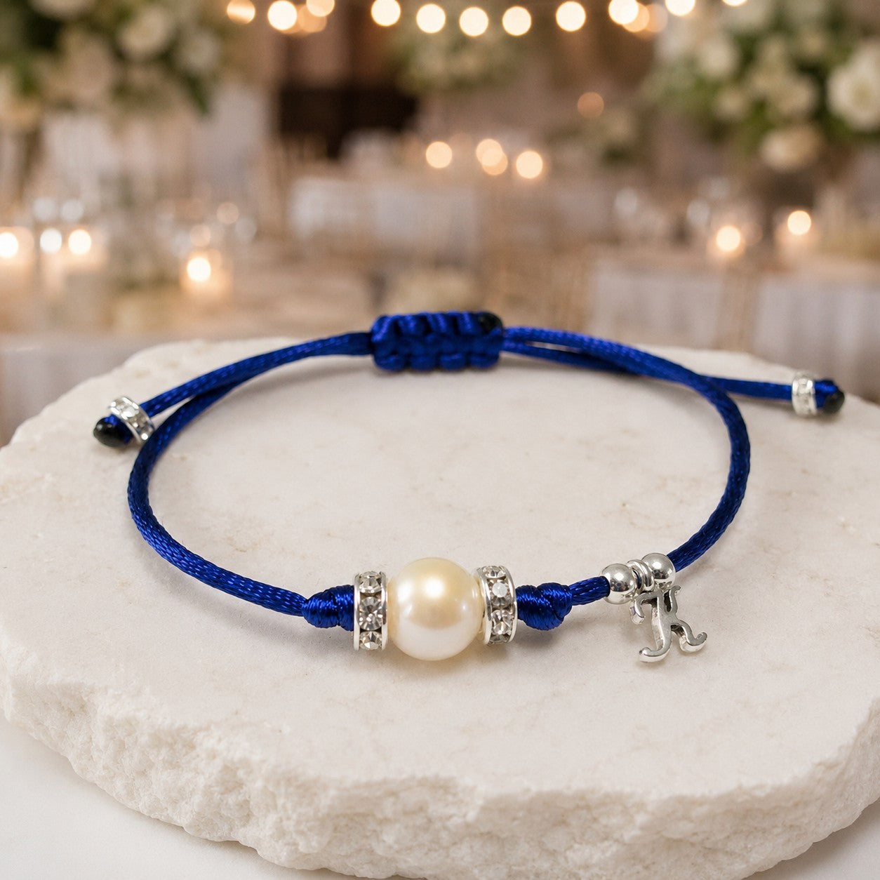 Elegant minimalist bracelet featuring a single natural white freshwater pearl centered between two rhinestone-studded silver rondelle spacers, strung on a vibrant royal blue nylon cord with sliding knot closure; includes a small silver initial charm for personalization and silver accent beads on the adjustable ends.