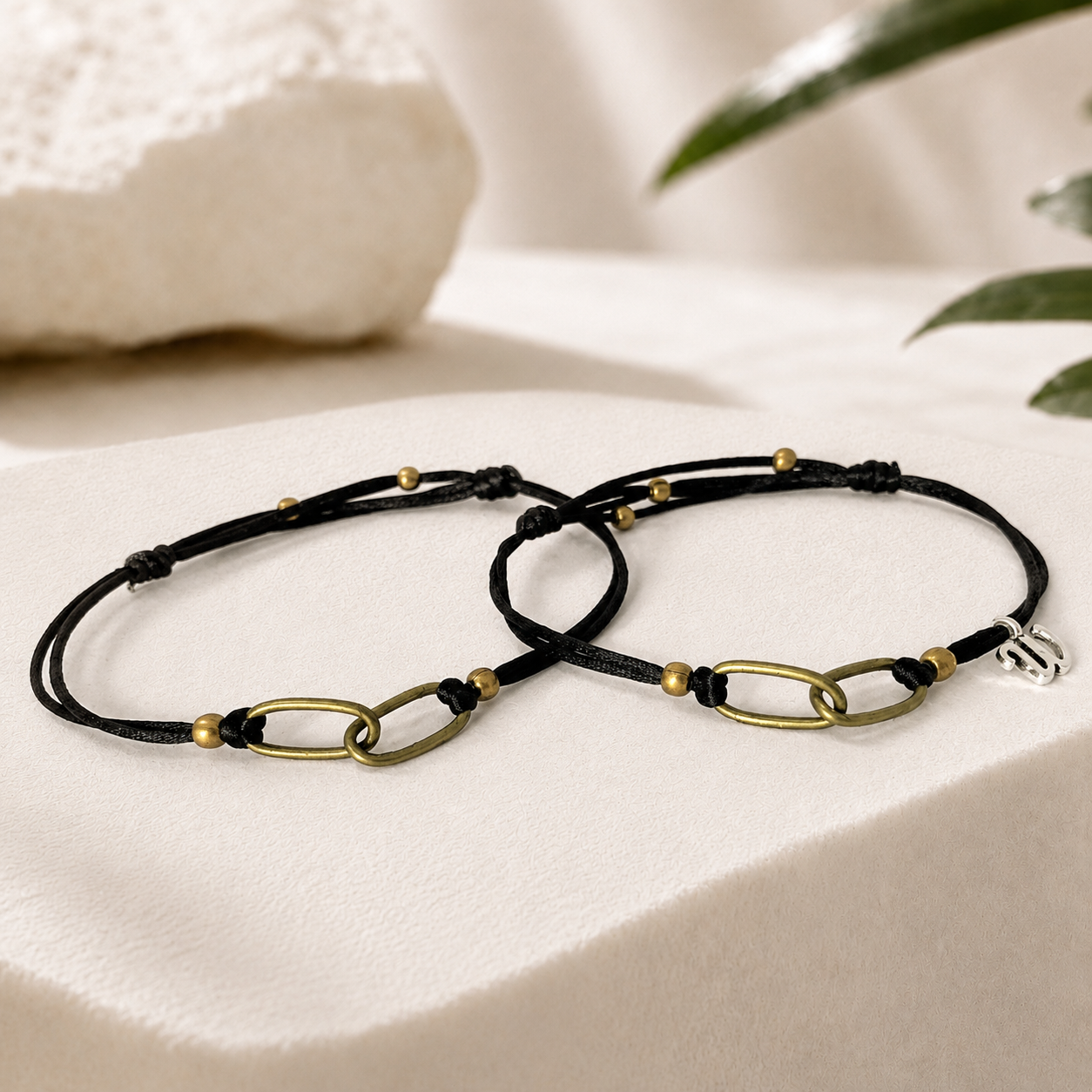 Father and son matching bracelets with black waterproof cord and interlocking antique brass chain links displayed on a luxury white stone background. Personalized family bond bracelet set, adjustable handmade jewelry gift for dad and son.