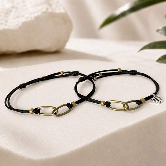Father and son matching bracelets with black waterproof cord and interlocking antique brass chain links displayed on a luxury white stone background. Personalized family bond bracelet set, adjustable handmade jewelry gift for dad and son.