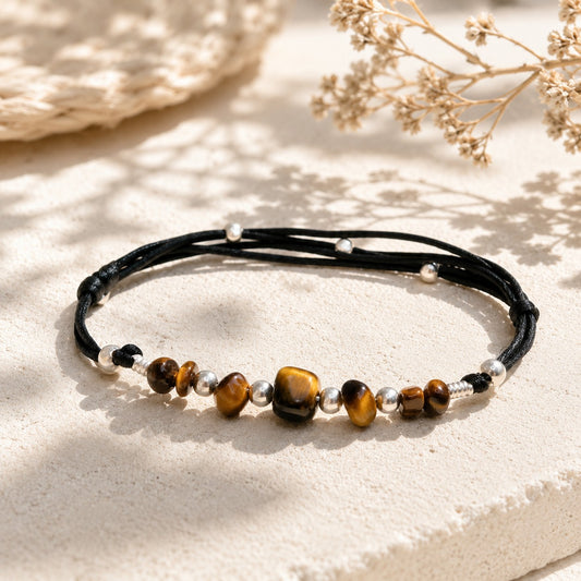 Handmade Tiger’s Eye anklet with polished brown-golden gemstone nuggets, accented by shiny silver beads on a black adjustable nylon cord. The anklet features a sliding knot clasp for a custom fit and an optional small initial charm. Presented gift-ready in a simple jewelry box.