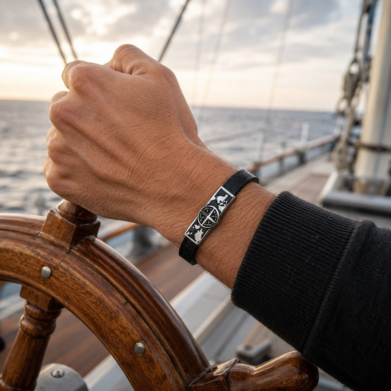 Men’s black leather compass bracelet with stainless steel world map charm worn aboard a sailing yacht. Travel-inspired leather bracelet featuring a magnetic clasp and compass design, symbolizing adventure, navigation, and freedom. Thoughtful gift for travelers, sailors, husbands, boyfriends, dads, and outdoor enthusiasts.