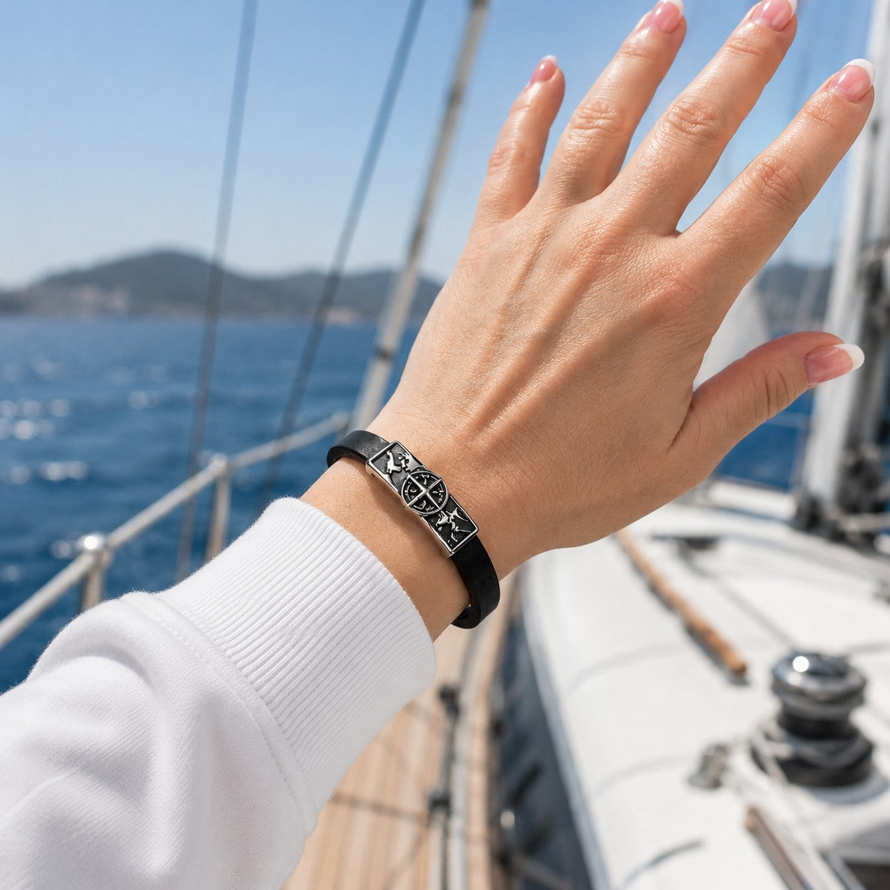Black leather world map bracelet worn on a woman's wrist aboard a luxury yacht, featuring a silver-tone compass and travel-inspired centerpiece. Styled with a casual white sweatshirt, this nautical bracelet is shown against a stunning ocean backdrop with sailboat details and blue water. Unisex travel jewelry with magnetic clasp, perfect for travelers, adventurers, cruise lovers, sailing enthusiasts, and meaningful gift giving. Handmade leather bracelet for men and women, ideal for vacations or travel.