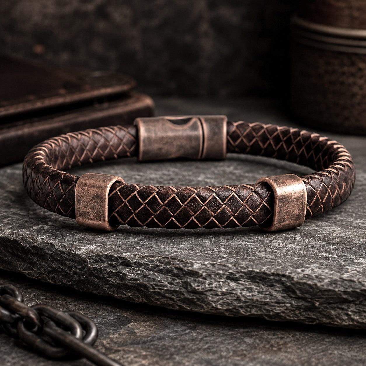 Luxury men's braided brown leather bracelet with antique copper magnetic clasp and copper accent rings displayed on a rugged dark stone surface. This handcrafted masculine leather bracelet features premium woven genuine leather, a secure magnetic closure, and a timeless rustic design. Styled with an industrial-inspired background of textured slate and metal accents, it is perfect as a gift for him, Father's Day, anniversary, birthday, Valentine's Day, Christmas, or everyday wear. 