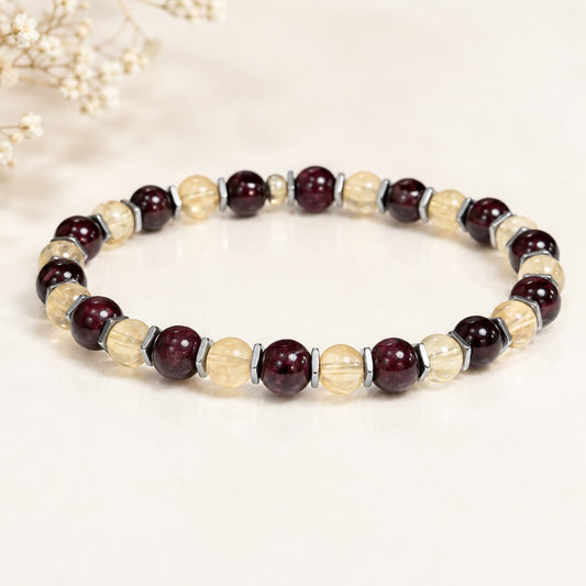 Handcrafted citrine and garnet stretch bracelet featuring alternating round beads of golden-yellow citrine and deep red garnet, separated by slim metallic hematite spacers. The bracelet is strung on a durable elastic cord for a comfortable, flexible fit. Displayed on a clean white background with subtle shadow, the contrasting warm and rich gemstone colors make this bracelet a bold yet elegant accessory for everyday wear or special occasions.