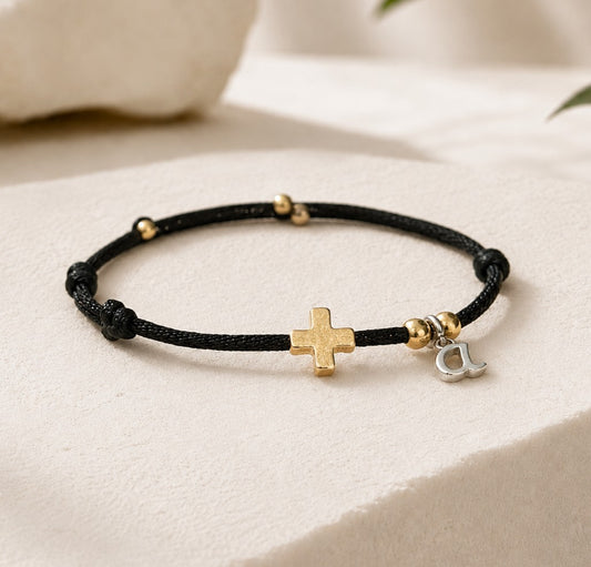 Black adjustable Christian cross bracelet with an 18K gold-filled cross, gold accent beads, black waterproof cord, and optional initial charm. Minimalist faith bracelet for men, women, and children.