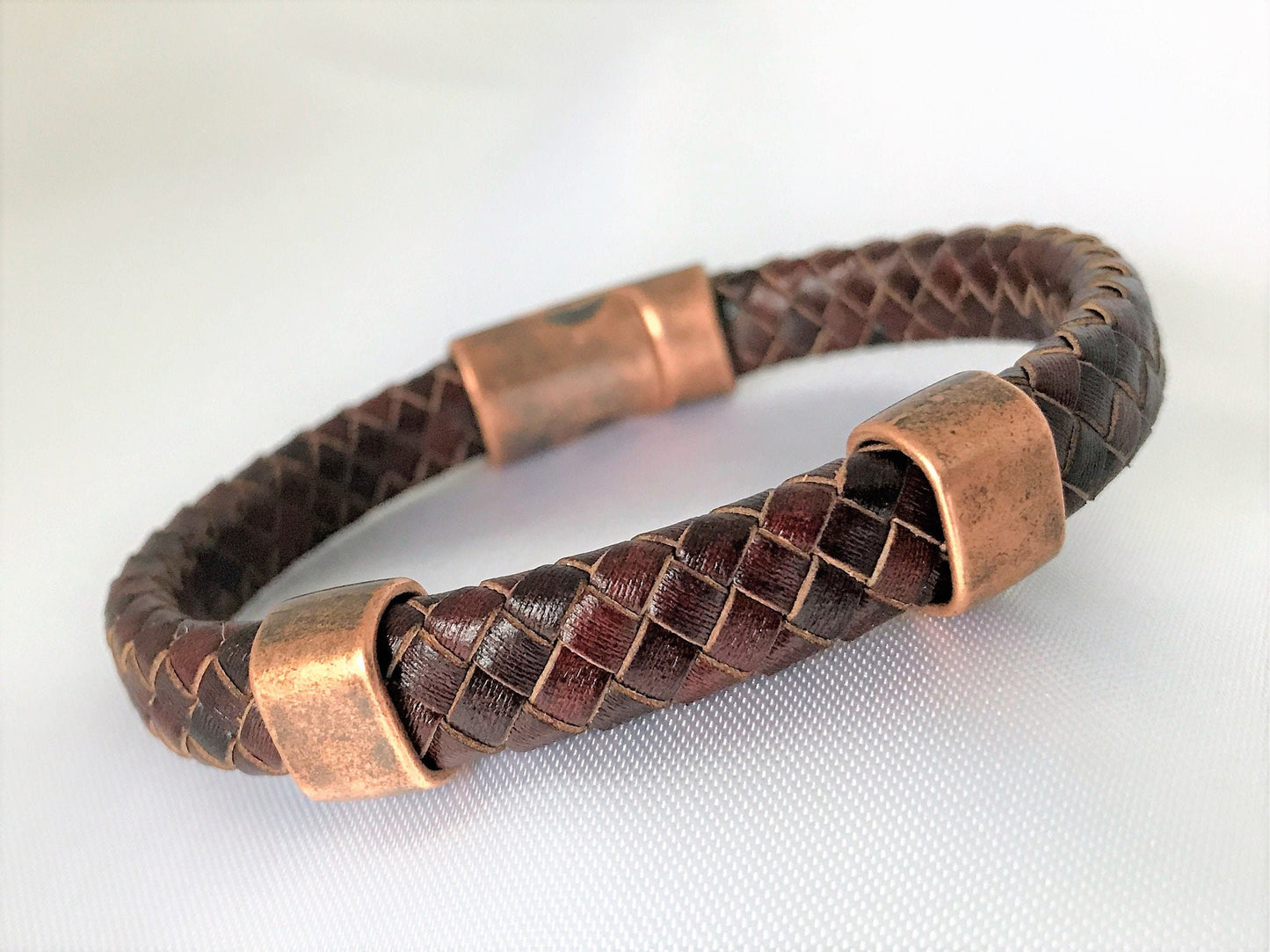 Beautifully flat folded braided genuine antique brown leather bracelet with 2 antique copper-plated sliders and antique copper magnetic clasp. Bracelet is on the hard side. Keeps a round form well.