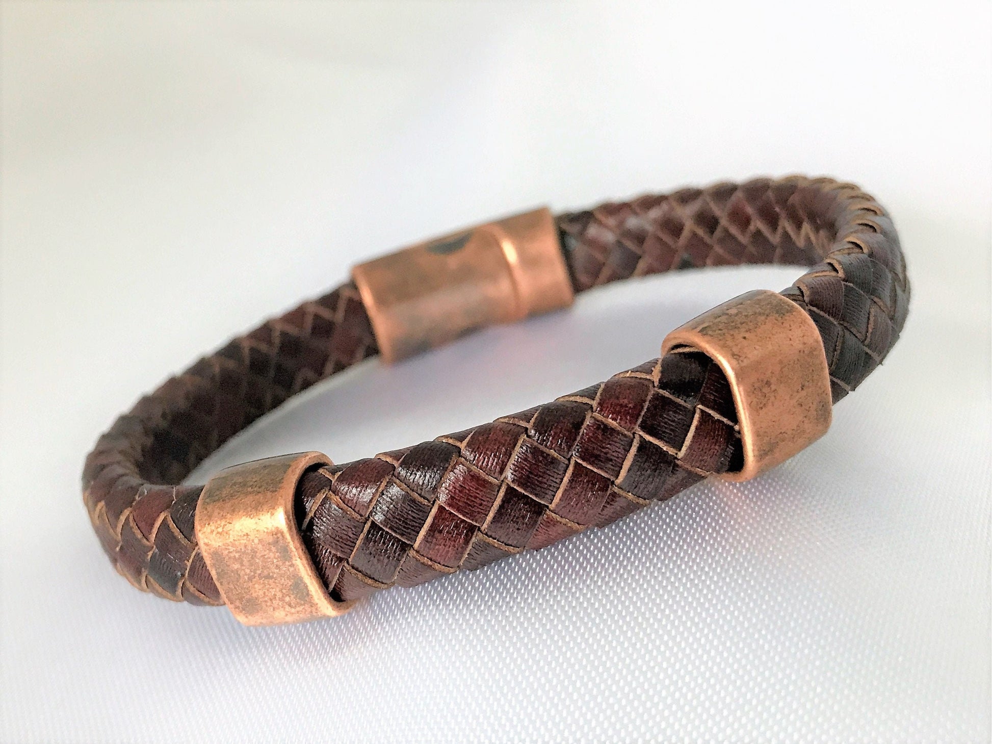 Beautifully flat folded braided genuine antique brown leather bracelet with 2 antique copper-plated sliders and antique copper magnetic clasp. Bracelet is on the hard side. Keeps a round form well.