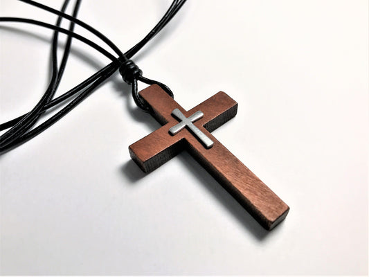 Wooden cross pendant with a silver center on a black cord against a white background