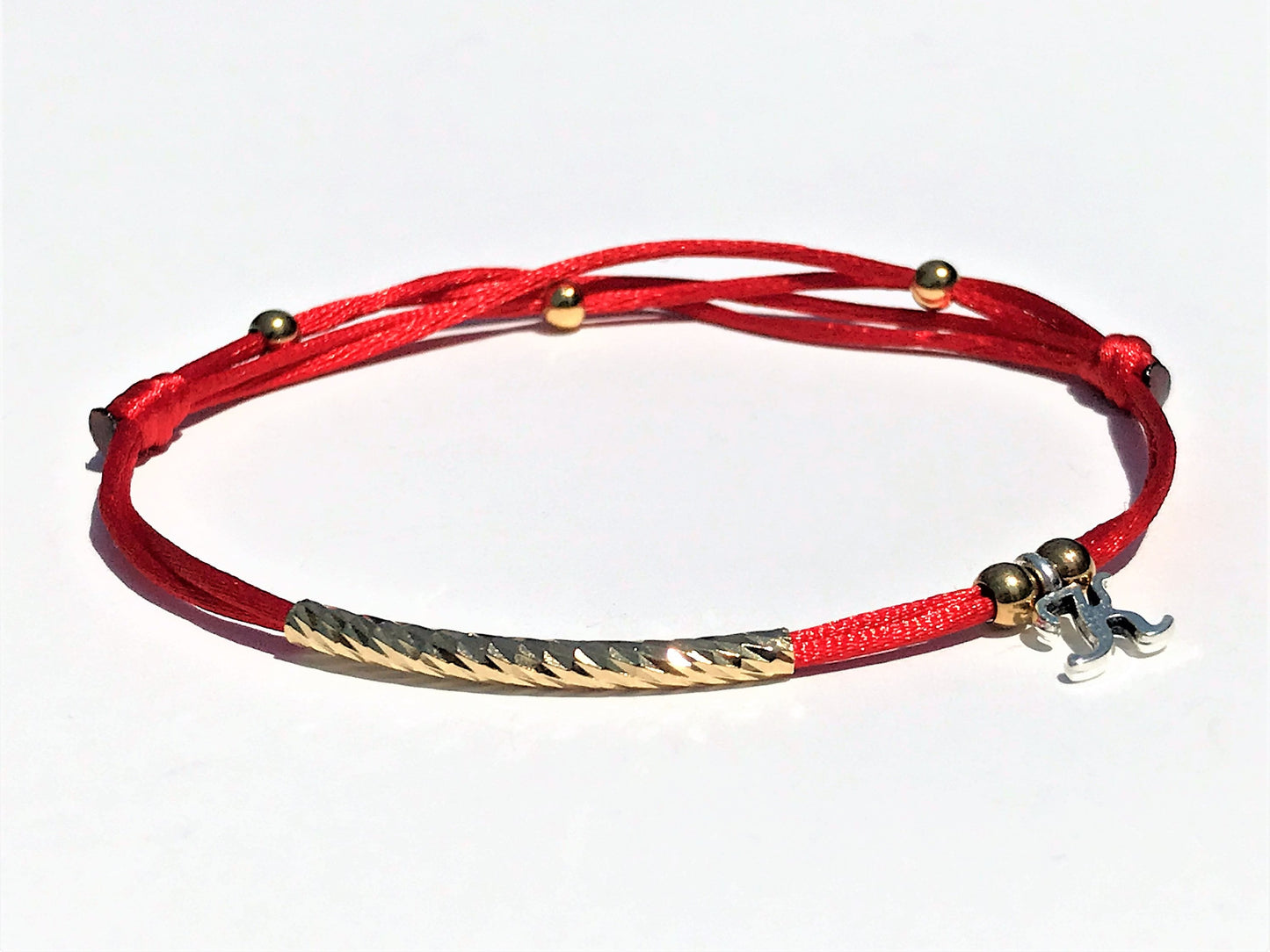 Handcrafted Adjustable Tiny Red String Bracelet for Good Luck. It features a silky red string complemented by a faceted gold tube and three delicate beads. Personalized with one initial surrounding by 2 gold bead