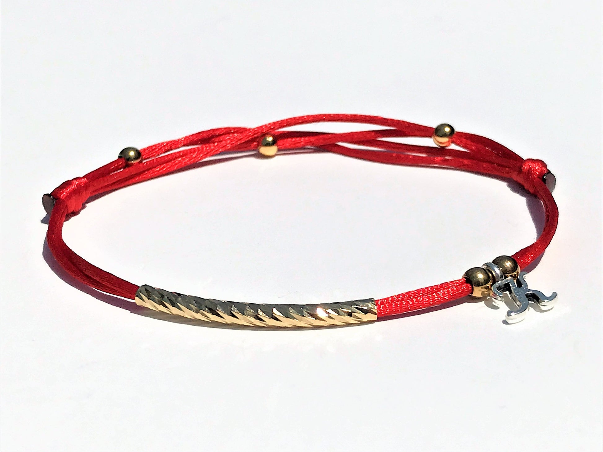 Handcrafted Adjustable Tiny Red String Bracelet for Good Luck. It features a silky red string complemented by a faceted gold tube and three delicate beads. Personalized with one initial surrounding by 2 gold bead