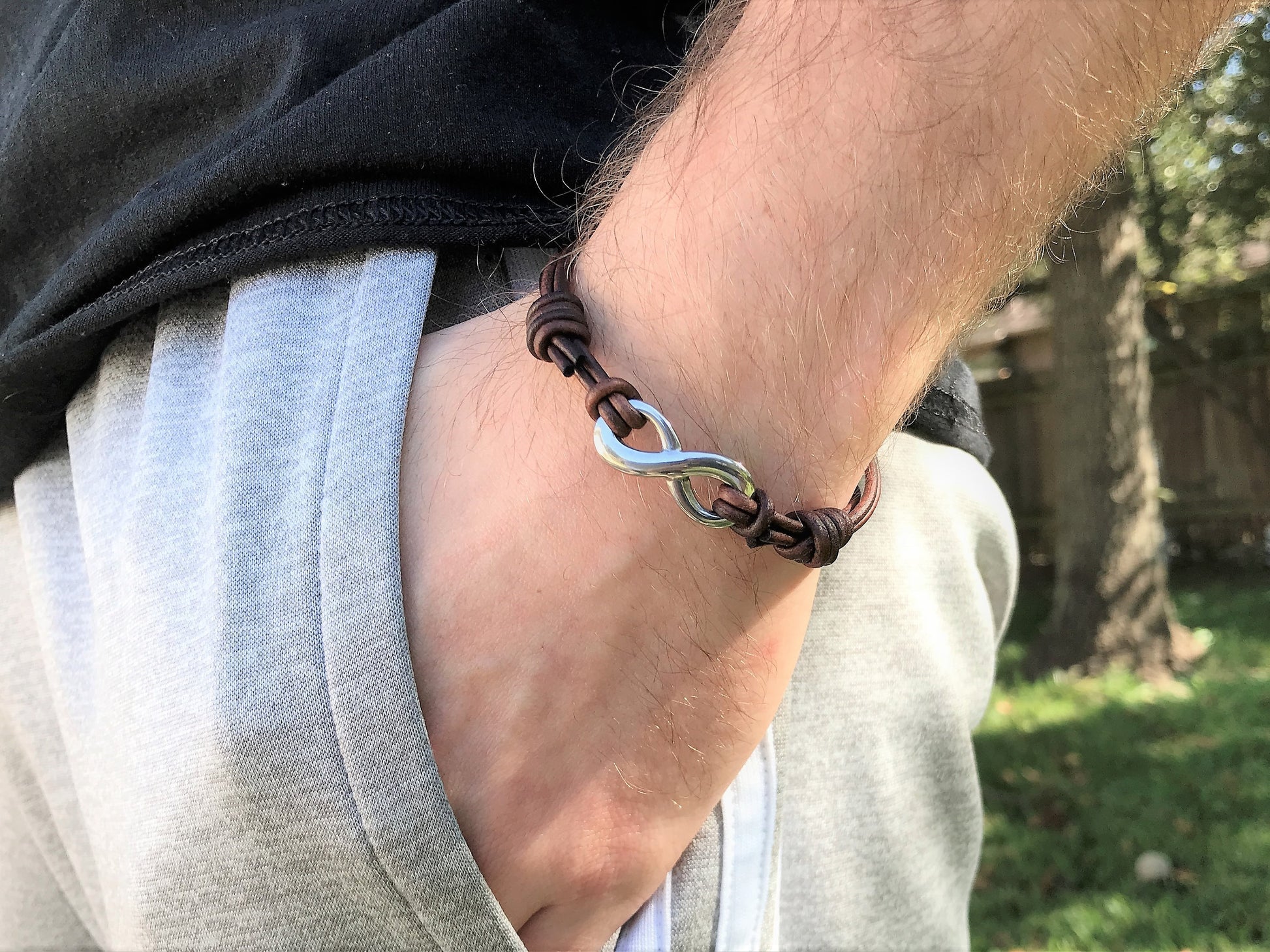 A person wearing an infinity  and distressed leather bracelet with a unique design outdoors