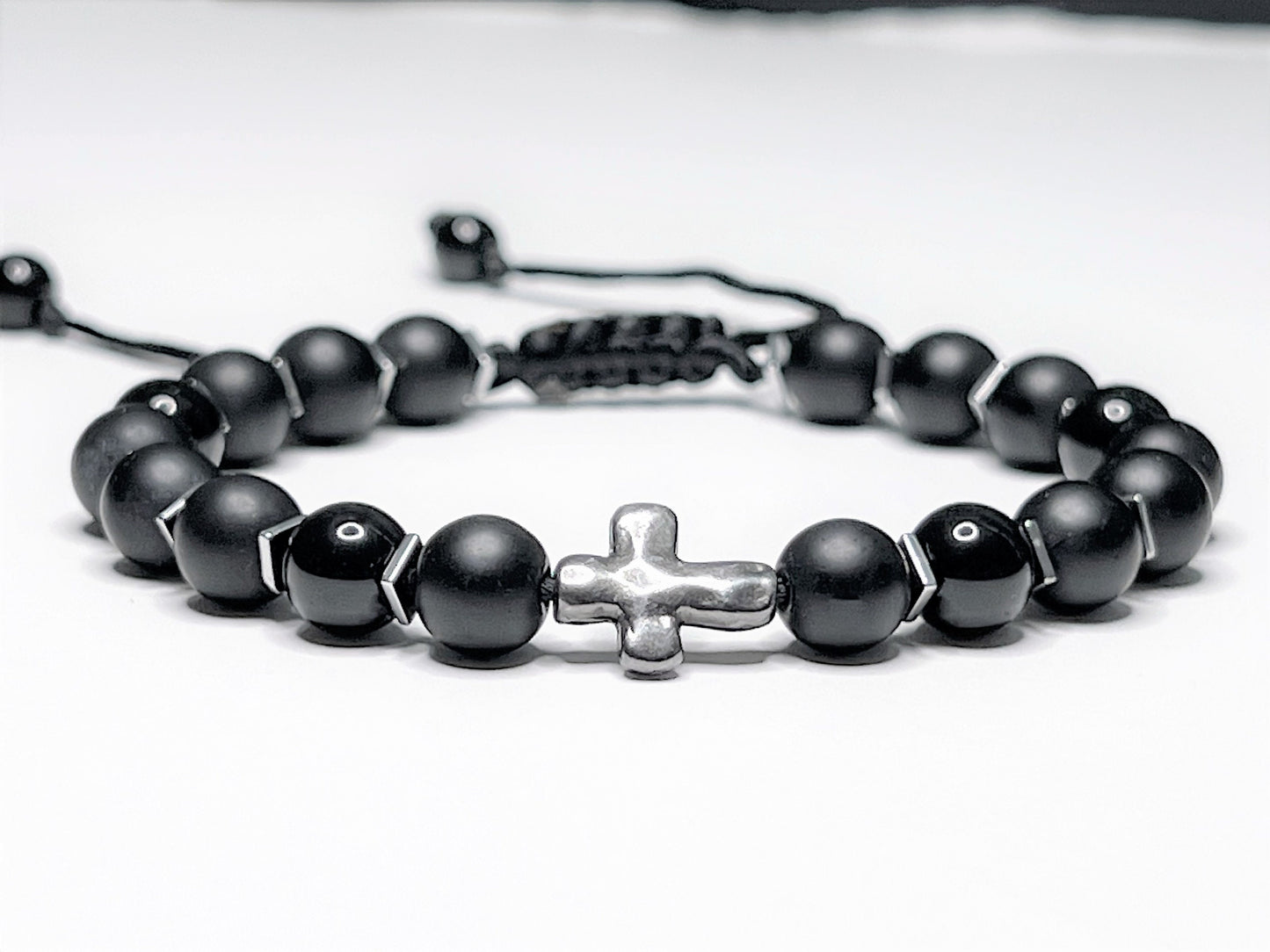 Adjustable black onyx beaded bracelet with silver hematite spacers and a central silver cross on a macramé nylon cord.