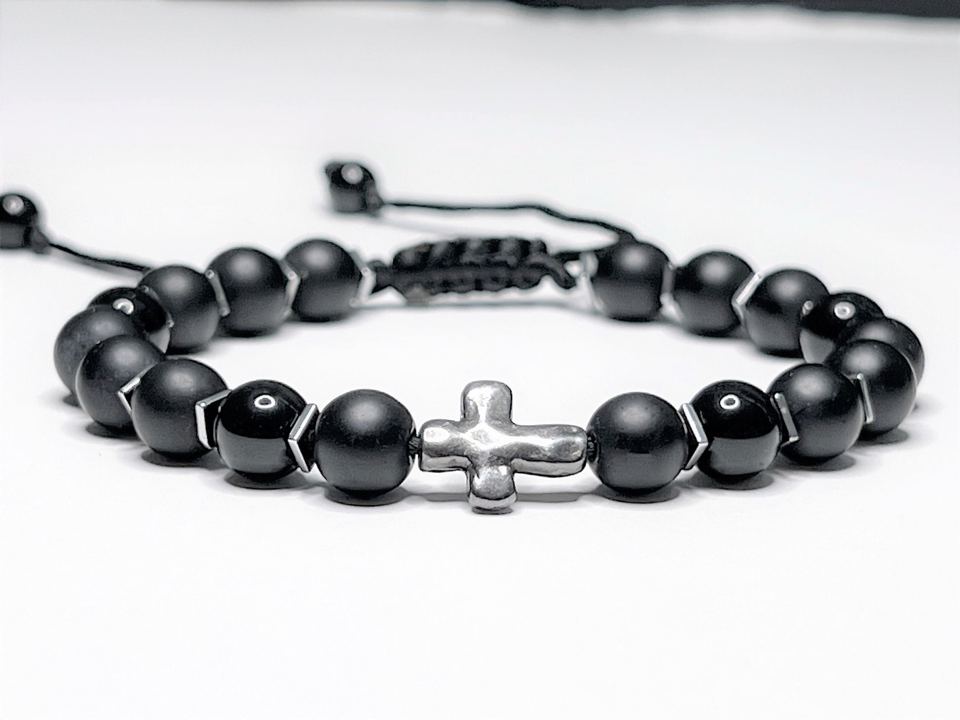 Adjustable black onyx beaded bracelet with silver hematite spacers and a central silver cross on a macramé nylon cord.