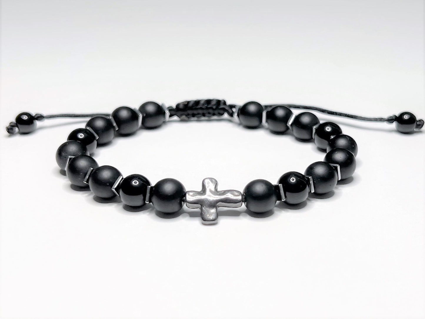 Adjustable black onyx beaded bracelet with silver hematite spacers and a central silver cross on a macramé nylon cord.