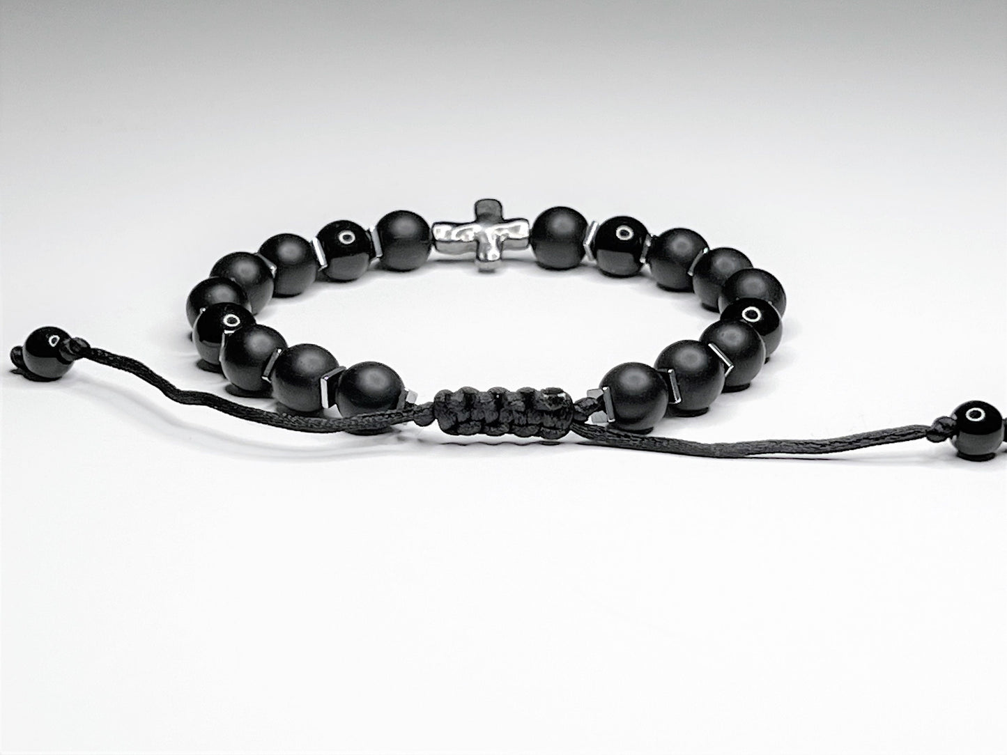 Close-up clasp of a Black onyx bracelet with silver hematite cubes and a silver cross, on an adjustable macramé cord.