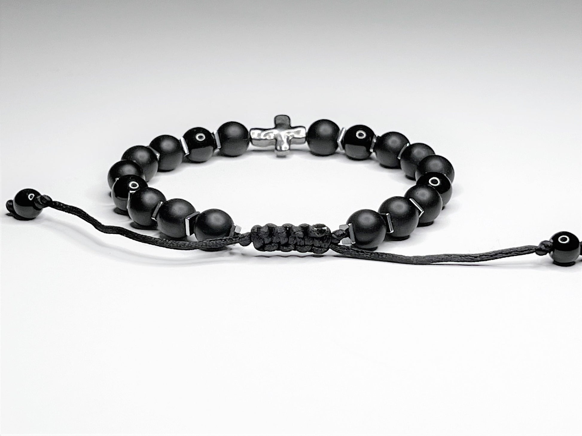 Close-up clasp of a Black onyx bracelet with silver hematite cubes and a silver cross, on an adjustable macramé cord.