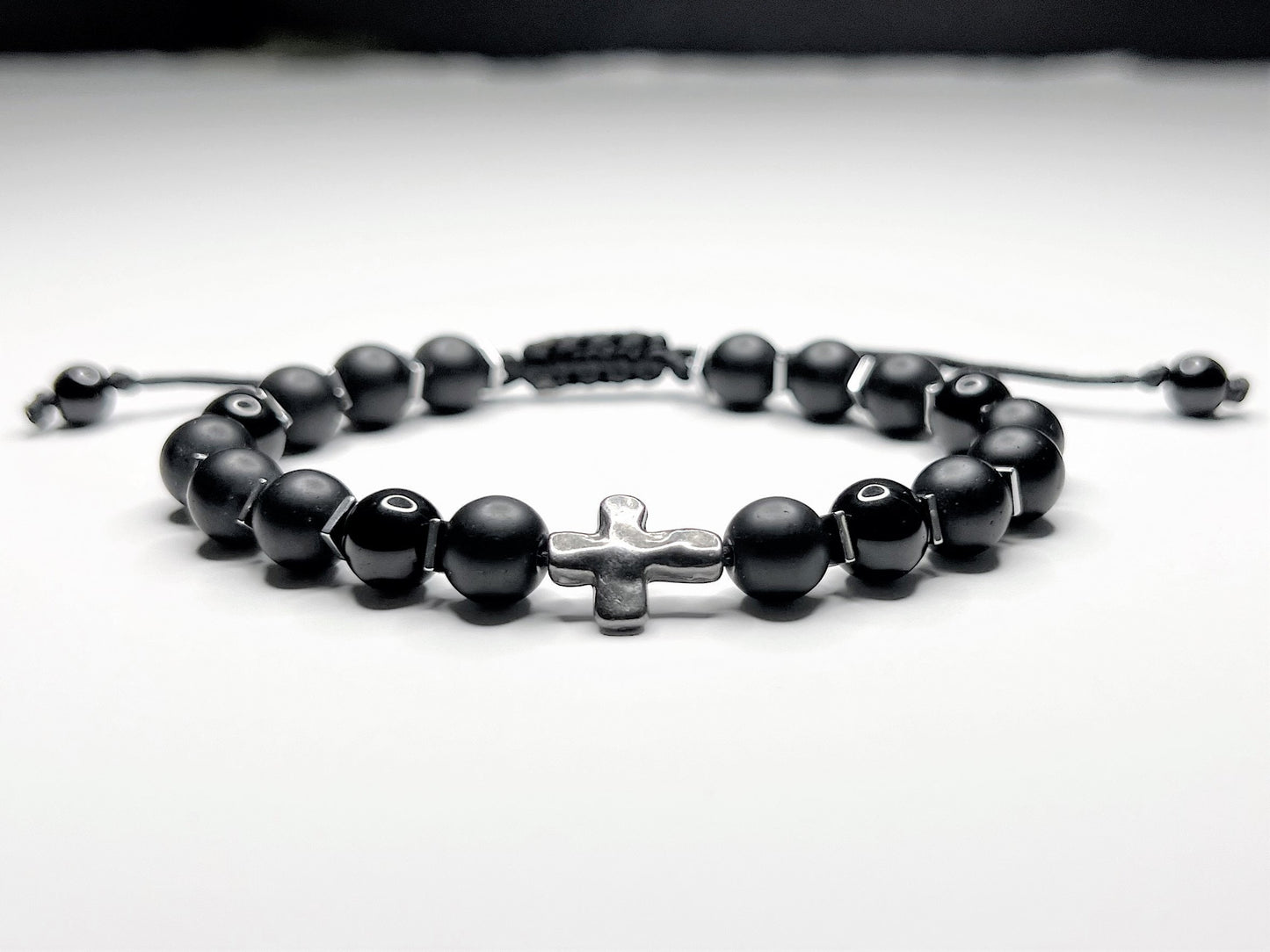 Black onyx bracelet with silver hematite cubes and a silver cross, on an adjustable macramé cord.