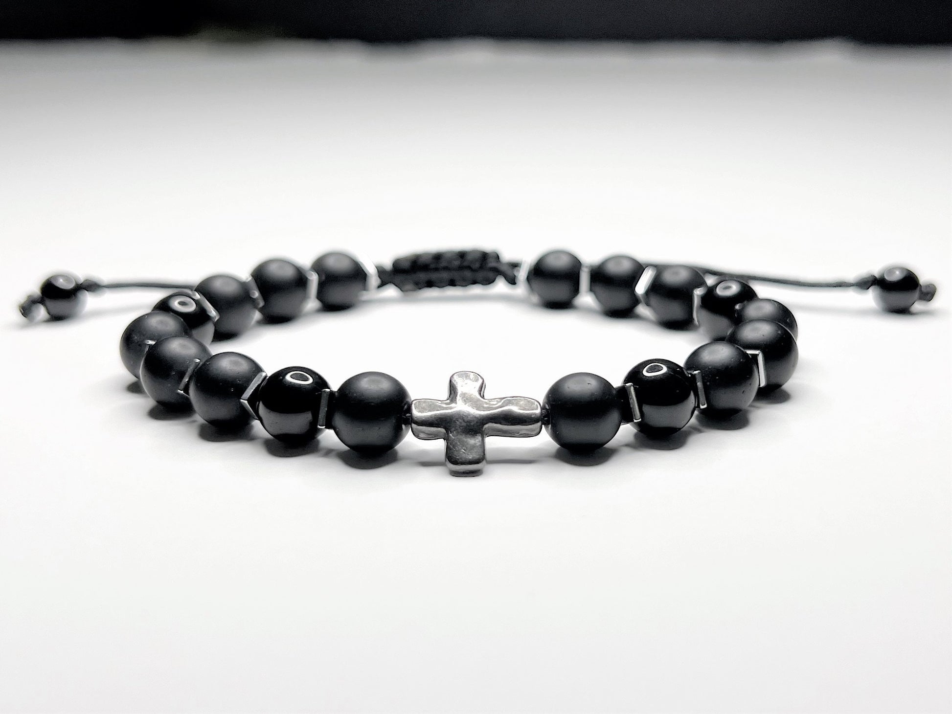 Black onyx bracelet with silver hematite cubes and a silver cross, on an adjustable macramé cord.