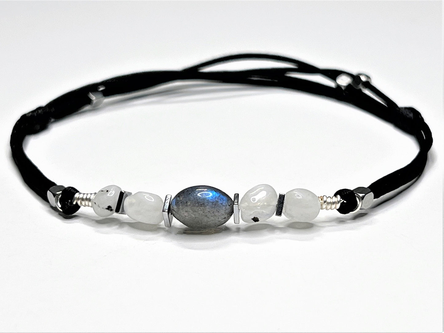 Moonstone and Labradorite gemstones anklet. The anklet is made with silky black string and adjustable for a perfect size.  
One big Labradorite surrounds smaller moonstone gemstones. In between gemstones, are square flat Hematite silver beads.