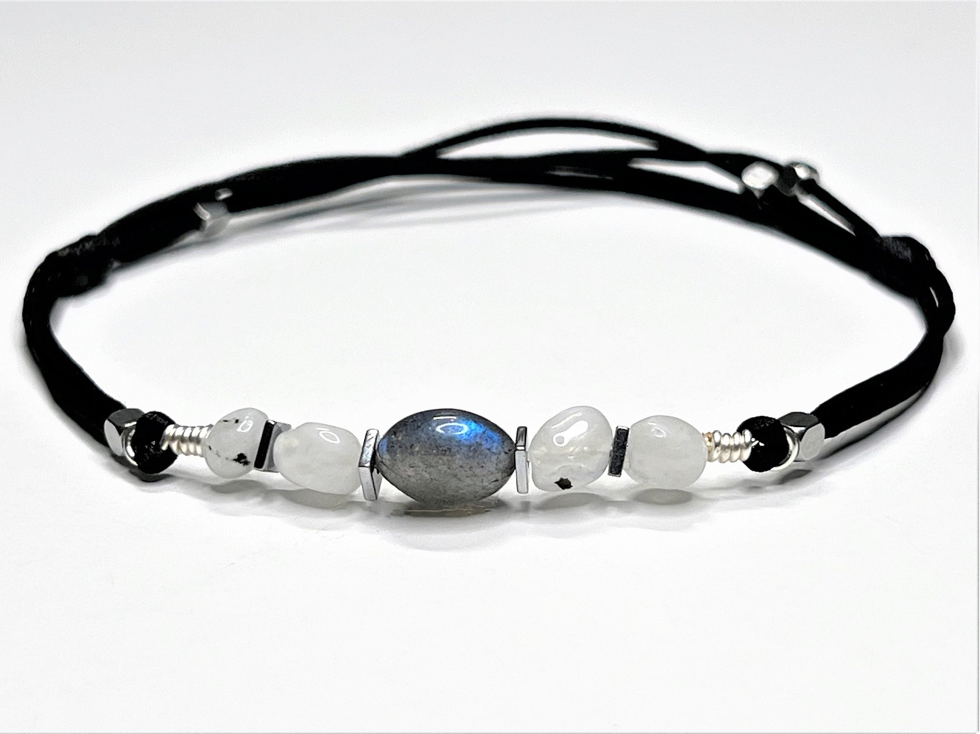 Moonstone and Labradorite gemstones anklet. The anklet is made with silky black string and adjustable for a perfect size.  
One big Labradorite surrounds smaller moonstone gemstones. In between gemstones, are square flat Hematite silver beads.