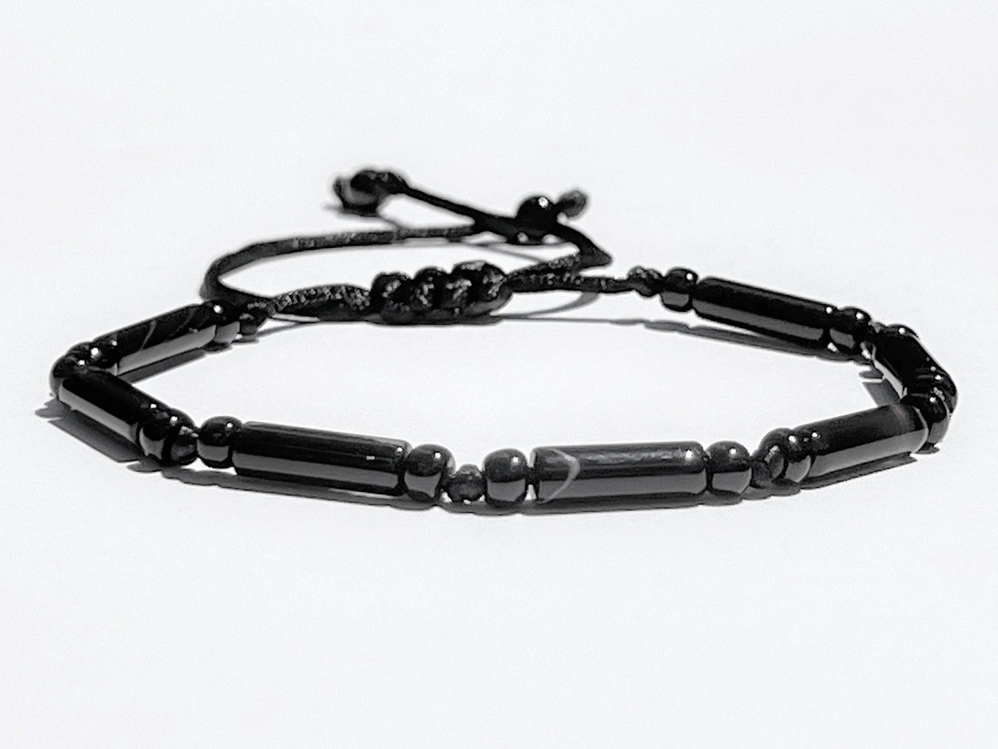 Black onyx tube bead bracelet with adjustable sliding knot cord on beige stone background, handmade unisex gemstone jewelry