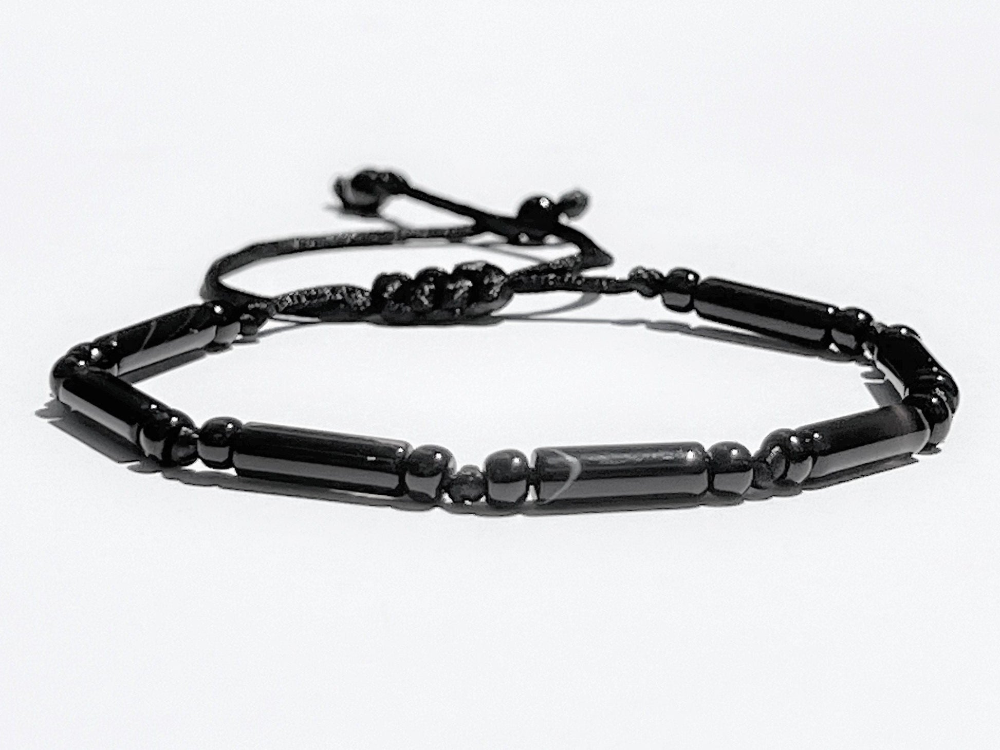Black onyx tube bead bracelet with adjustable sliding knot cord on beige stone background, handmade unisex gemstone jewelry