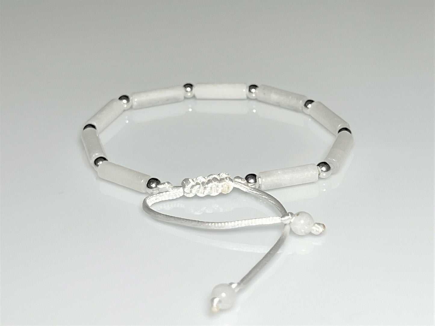 Close-up clasp of White jade tube bead bracelet with silver accents on an adjustable white cord.