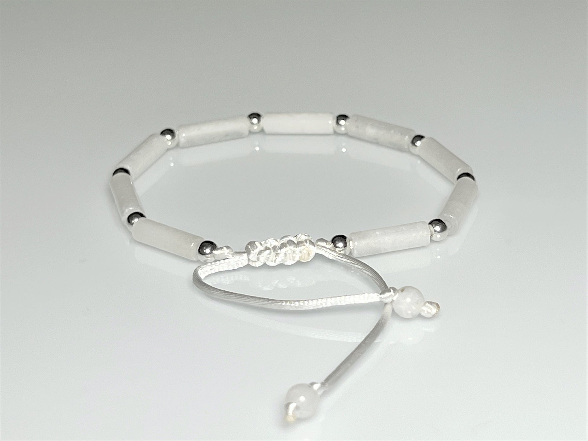 Close-up clasp of White jade tube bead bracelet with silver accents on an adjustable white cord.