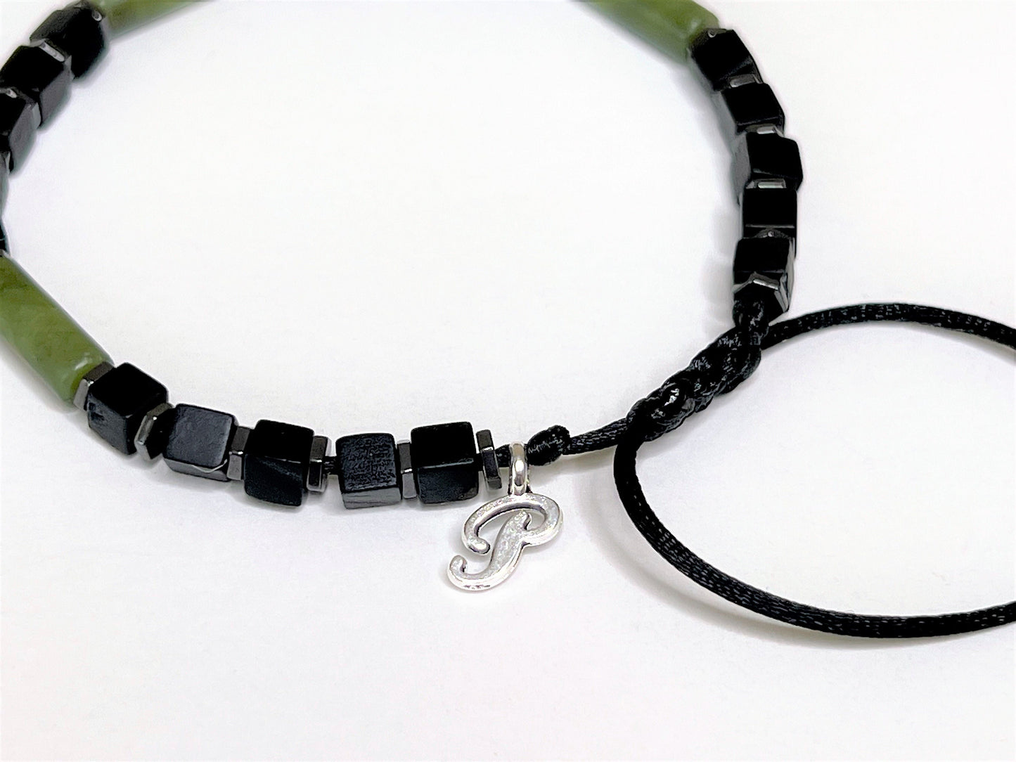 Side view of a green jade and matte-black cubic onyx bracelet. Personalized with one initial charm. With black beads and a silver 'P' charm on a white background
