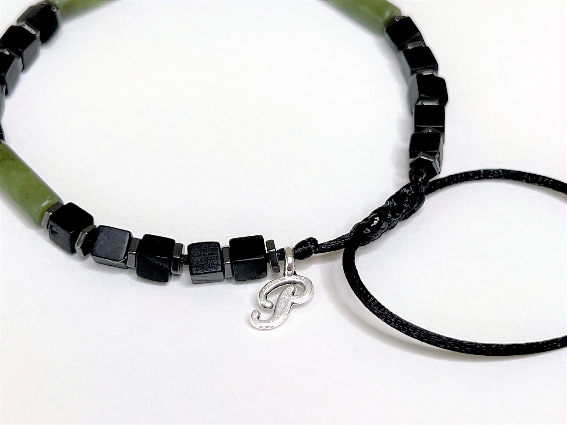 Side view of a green jade and matte-black cubic onyx bracelet. Personalized with one initial charm. With black beads and a silver 'P' charm on a white background