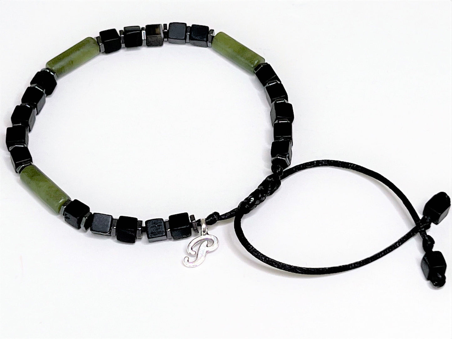 Side view of an adjustable handmade bracelet featuring a central cylindrical green jade bead flanked by matte black cubic onyx and faceted hematite spacer beads. Personalized with one initial charm.