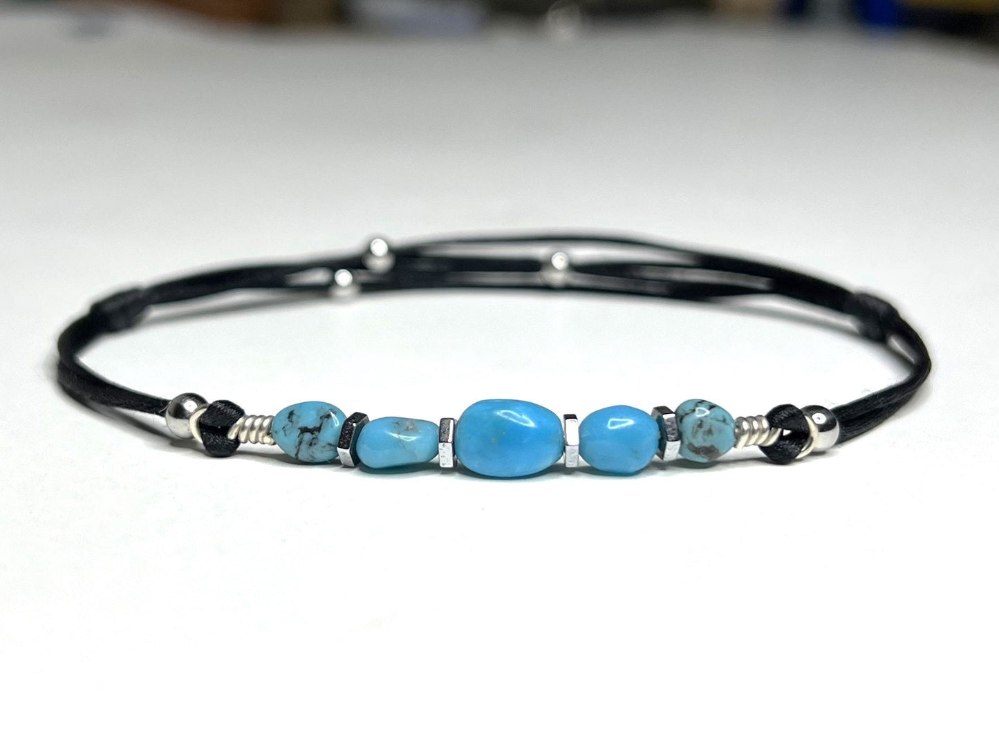 Close-up Adjustable and waterproof anklet. I use natural, untreated Turquoise nuggets and silver hematite beads on a black, silky nylon cord. A total of 5 gemstones,  in the center, a larger gemstone. Each stone is embellished with hematite beads around it.