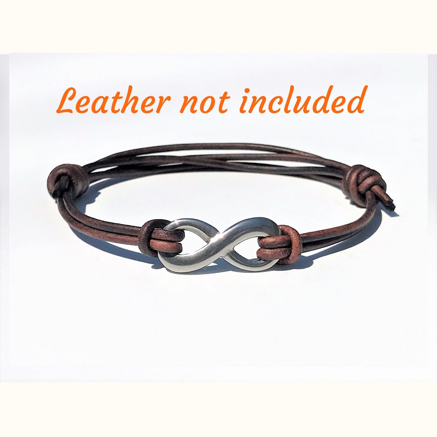 Bracelet with silver infinity symbol and brown leather strap on a white background with text 'Leather not included'.