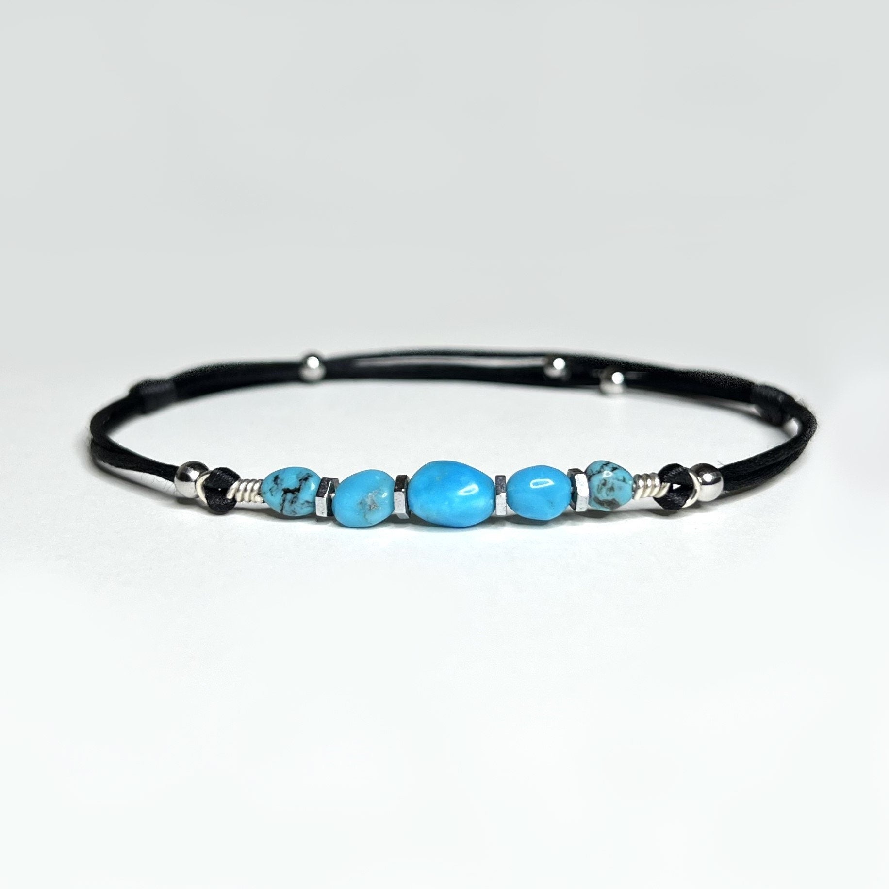 Adjustable and waterproof anklet. I use natural, untreated Turquoise nuggets and silver hematite beads on a black, silky nylon cord. A total of 5 gemstones,  in the center, a larger gemstone. Each stone is embellished with hematite beads around it.