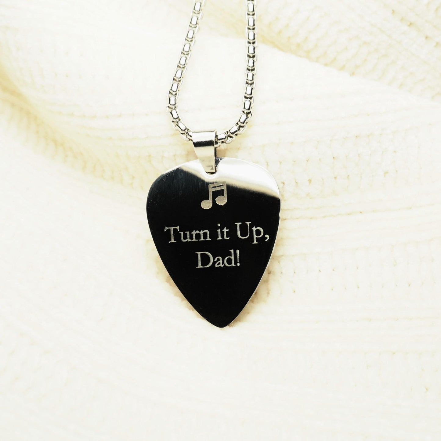 Back side of guitar pick necklace showing custom engravings of "Turn it up, Dad!"