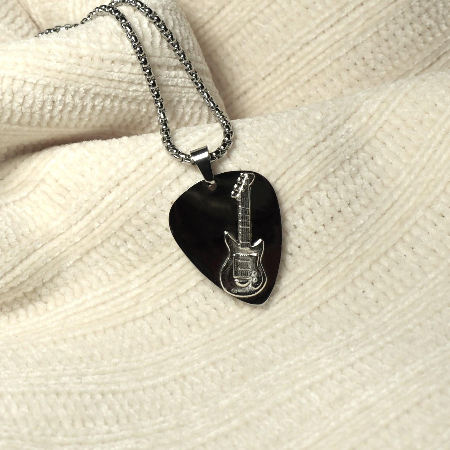 Guitar pick-shaped pendant with guitar design on a chain.