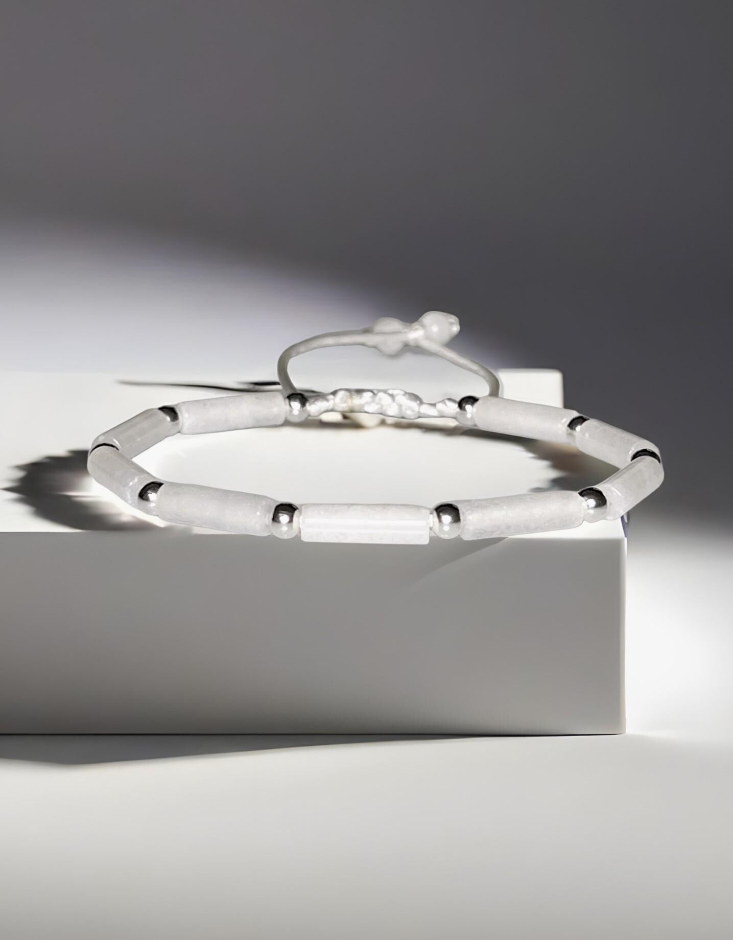 White jade tube bead bracelet with silver accents on an adjustable white cord.
