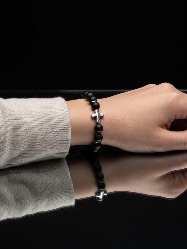 Adjustable black bead and silver cross bracelet shown on a person's wrist, reflecting minimalist religious style and elegance.