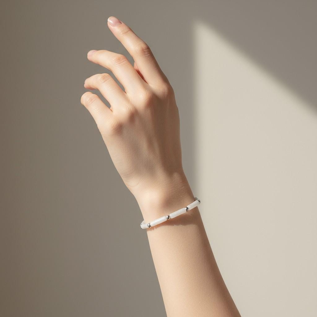 A hand wearing a bracelet. Delicate bracelet with white jade tube beads and silver accents on an adjustable white cord.