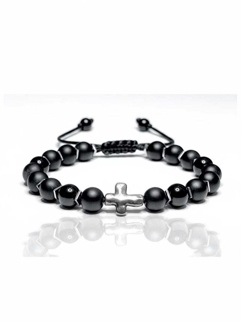 Handmade adjustable bracelet featuring matte and glossy black onyx beads, accented with silver-toned hematite cube spacers and a central silver cross bead. The beads are strung on durable black nylon cord with a macramé sliding knot closure, adjustable from 6 to 9 inches. Photographed on a clean white background, the bracelet showcases a bold and spiritual design, ideal for men or women as a religious or meaningful gift.