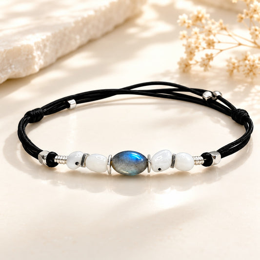 Handmade Labradorite and Moonstone anklet on an elegant ivory background featuring a blue-flash Labradorite gemstone, white Moonstone beads, silver-tone spacers, and waterproof adjustable black cord. Luxury boho gemstone anklet for women, beach jewelry, summer fashion, minimalist style, everyday wear, and gift giving.