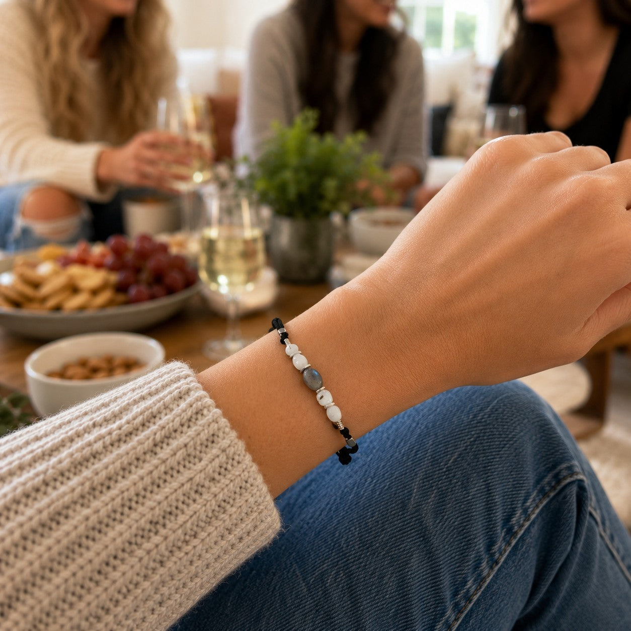 Handmade Labradorite and moonstone adjustable bracelet on a woman's wrist at a casual home gathering. Features genuine labradorite with blue flash, natural moonstone beads, hematite accents, and a waterproof, adjustable cord. Personalized gemstone bracelet for women, perfect as a birthday gift, anniversary gift, friendship bracelet, bridesmaid jewelry, or everyday crystal bracelet.