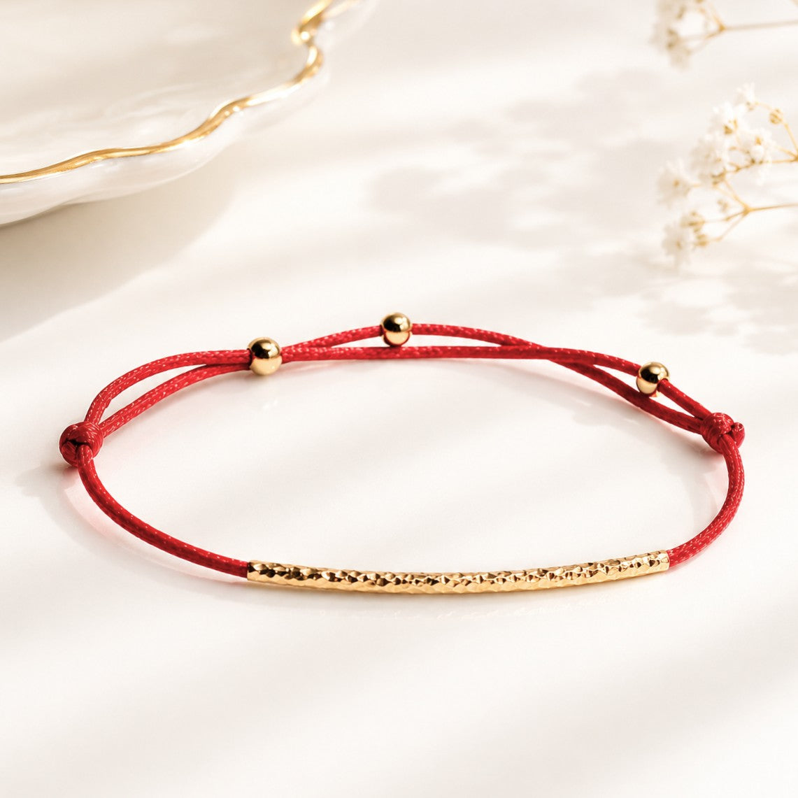 Handcrafted Adjustable Tiny Red String Bracelet for Good Luck. It features a silky red string complemented by a faceted gold tube and 3 delicate beads. Personalize it with 1 initial charm—a perfect blend of elegance and meaning.