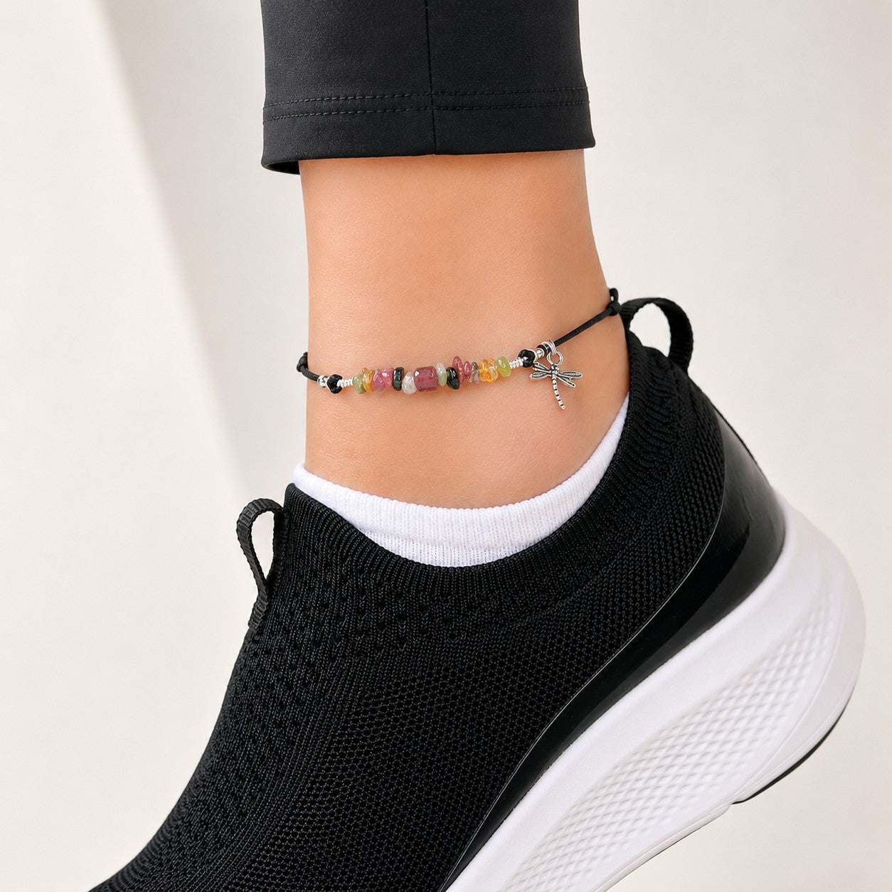 Adjustable gemstone anklet featuring a black cord design accented with polished silver-tone beads and a delicate silver dragonfly charm. The center of the anklet showcases a colorful arrangement of natural gemstone chips in shades of pink, green, yellow, black, clear, and watermelon tones, creating a vibrant and earthy look. The minimalist sliding-cord closure allows for a comfortable, customizable fit, while the genuine gemstone beads add a unique bohemian touch. Lightweight and versatile, this handcrafted